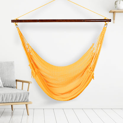 Yellow Jumbo Caribbean Hammock Chair hanging indoors beside a pale wood armchair against a white wall