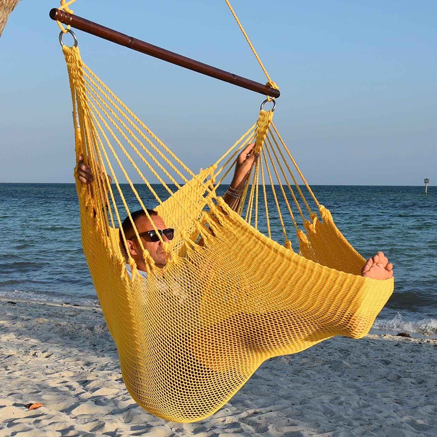 Man in sunglasses stretched out in a yellow Jumbo Caribbean Hammock Chair with calm ocean behind
