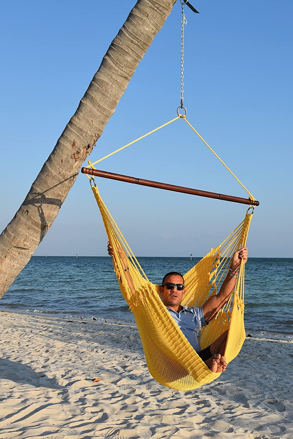 Man relaxing in a yellow Jumbo Caribbean Hammock Chair hung from a leaning palm tree on a beach