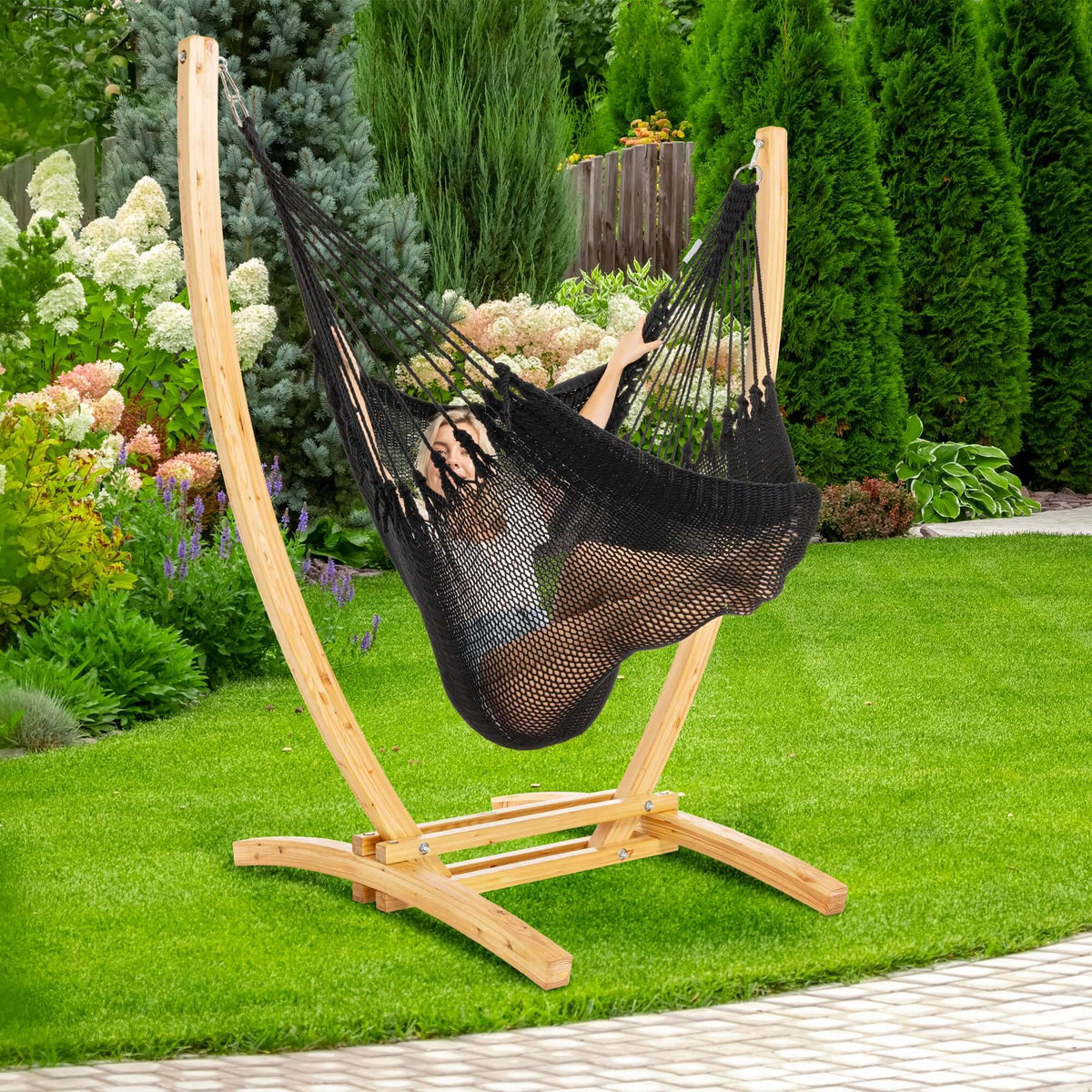 Black Jumbo Caribbean Recliner on a wood arc stand in a backyard beside flowering hydrangeas