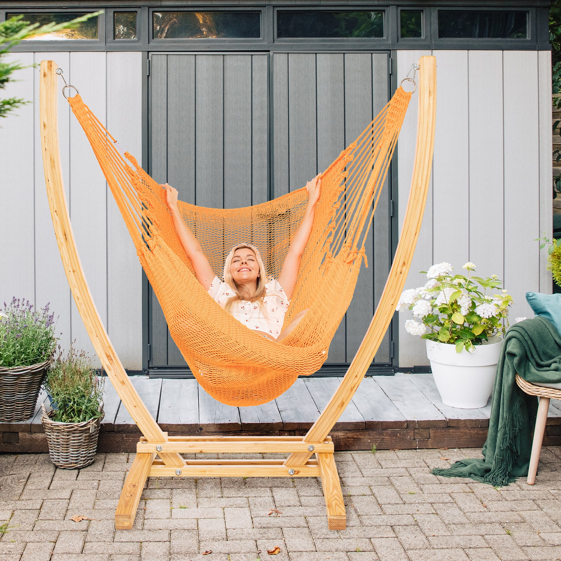 Orange Jumbo Caribbean Recliner on a wood arc stand on a brick paver patio in front of a grey garden shed