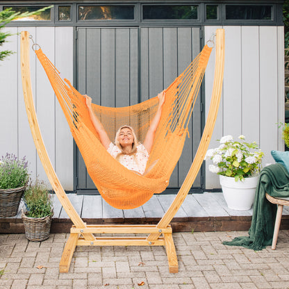 Orange Jumbo Caribbean Recliner on a wood arc stand on a brick paver patio in front of a grey garden shed