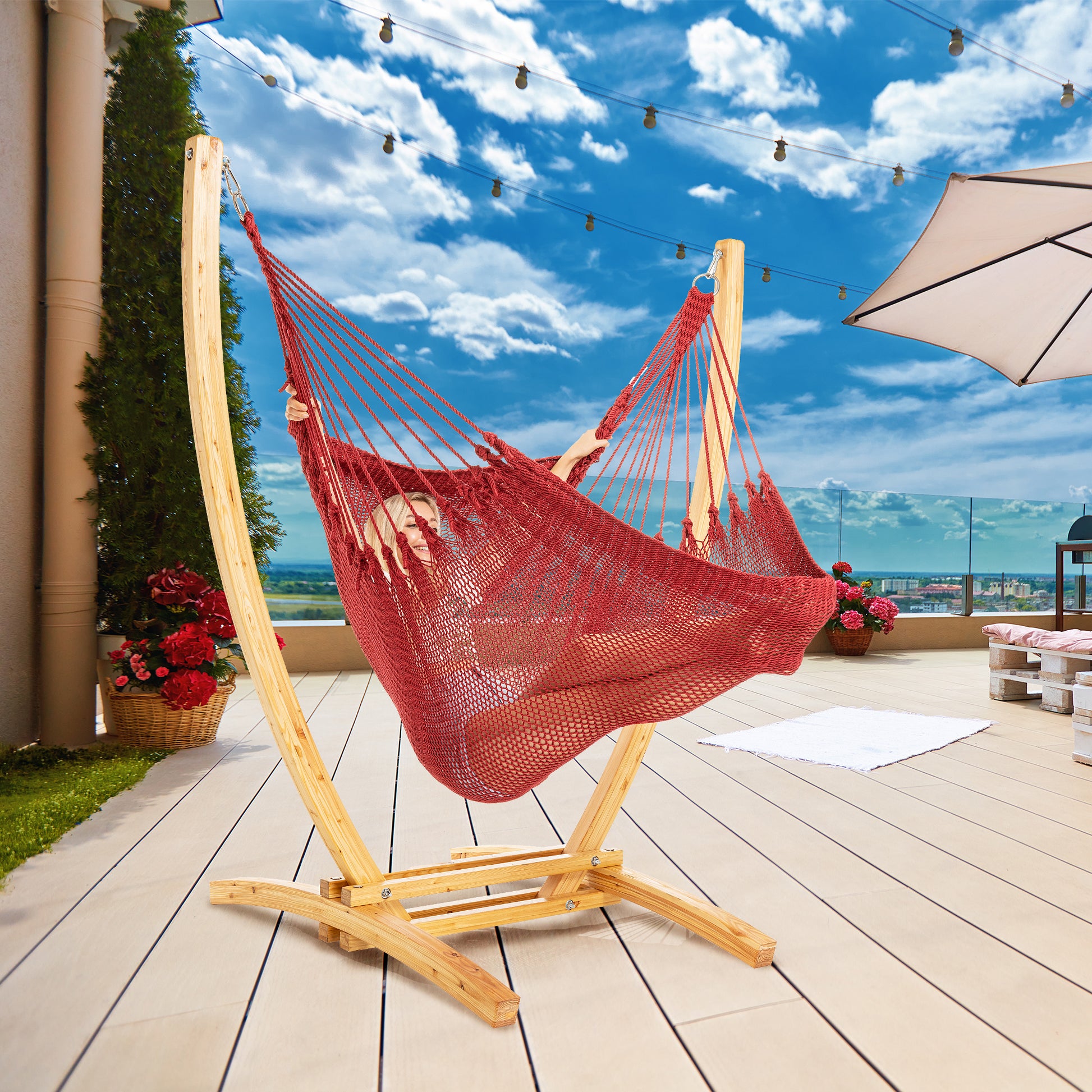 Red Jumbo Caribbean Recliner on a wood arc stand on a rooftop deck under string lights and a patio umbrella