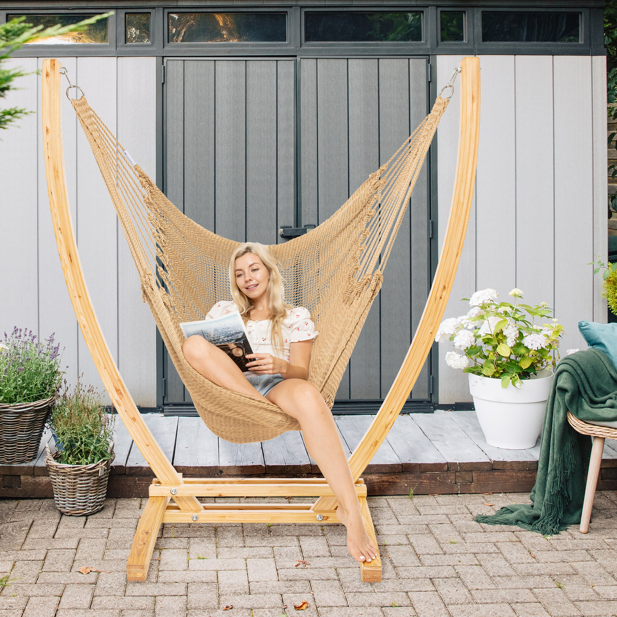 Tan Jumbo Caribbean Recliner on a wood arc stand on a brick paver patio in front of a grey garden shed