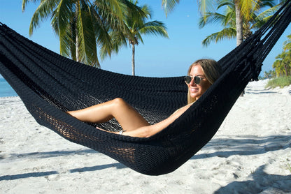 Woman reclining in the Black Jumbo Mayan Hammock, the deep hand-woven bed cradling her on the beach
