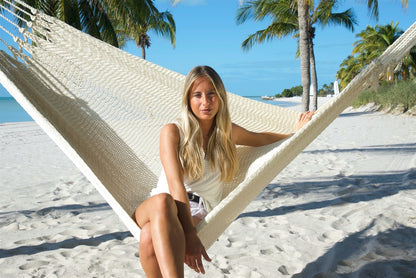 Woman sitting upright facing the camera in the Cream Jumbo Mayan Hammock on the beach