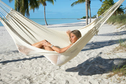Woman lying back in the Cream Jumbo Mayan Hammock, the deep polyester bed hugging her on a palm-lined beach
