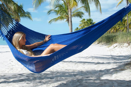 Woman reclining in the Dark Blue Jumbo Mayan Hammock on a palm-lined beach