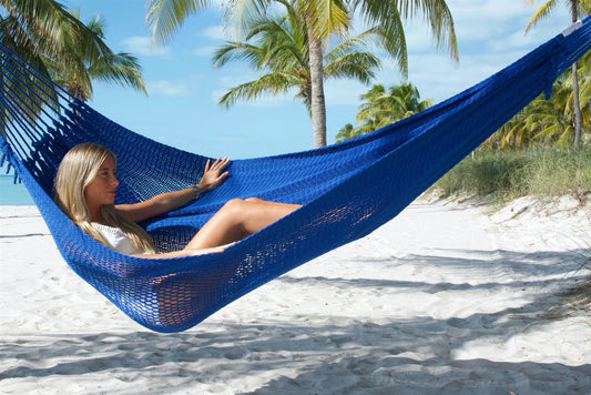 Woman reclining in the Dark Blue Jumbo Mayan Hammock on a palm-lined beach