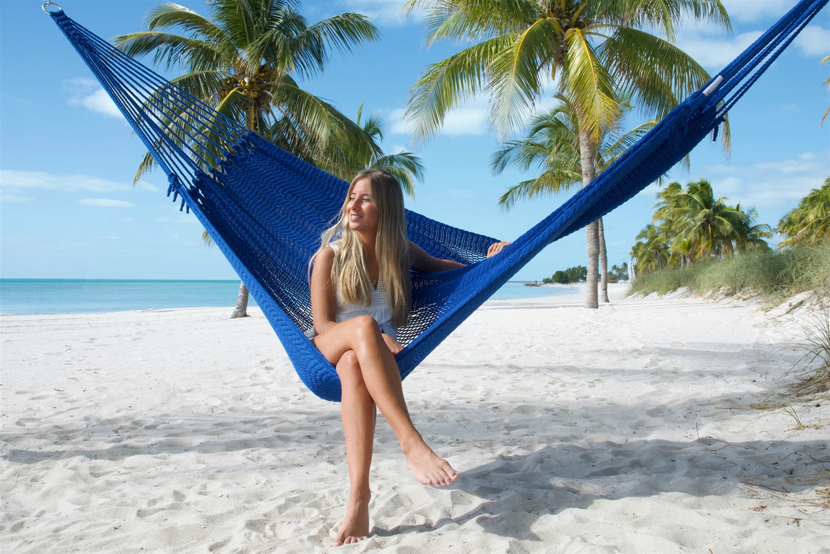 Woman sitting upright in the Dark Blue Jumbo Mayan Hammock with her legs crossed, palm trees behind