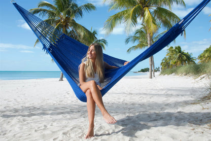 Woman sitting upright in the Dark Blue Jumbo Mayan Hammock with her legs crossed, palm trees behind