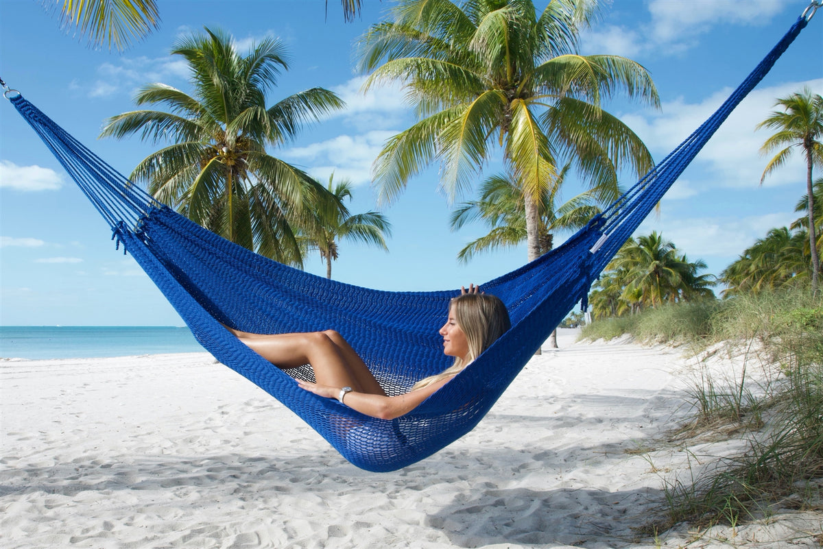 Dark Blue Jumbo Mayan Hammock hung between palms on the beach with a woman lying back in the bed