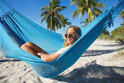 Woman reclining in the Light Blue Jumbo Mayan Hammock, the deep polyester bed cradling her on the beach