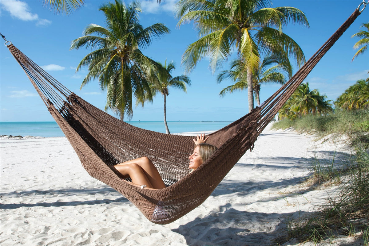 Mocha Jumbo Mayan Hammock hung between palms on the beach with a woman lying back in the bed