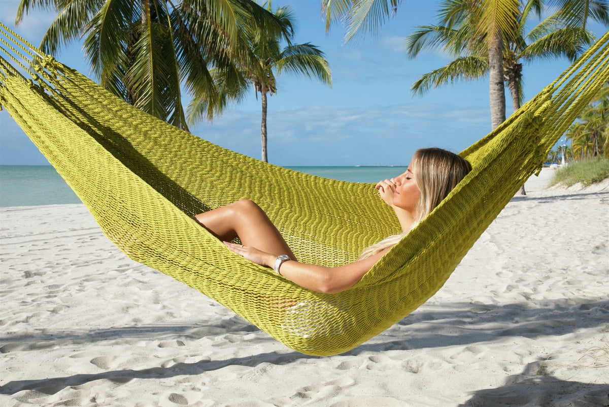 Woman lying back in the Olive Jumbo Mayan Hammock on a palm-lined beach