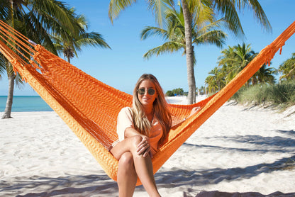 Woman sitting upright facing the camera in the Orange Jumbo Mayan Hammock on the beach