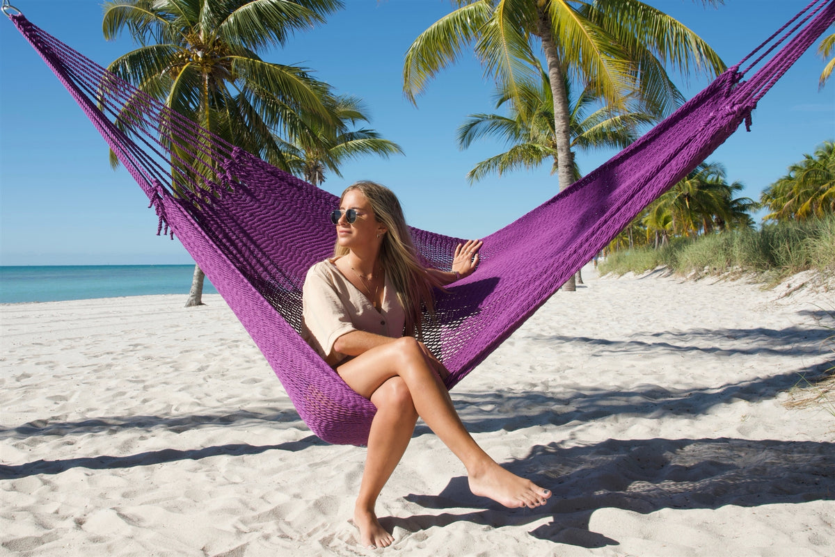 Woman sitting upright facing the camera in the Purple Jumbo Mayan Hammock on the beach