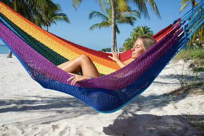 Woman lying back in the Rainbow Jumbo Mayan Hammock on the beach, showing its bands of color