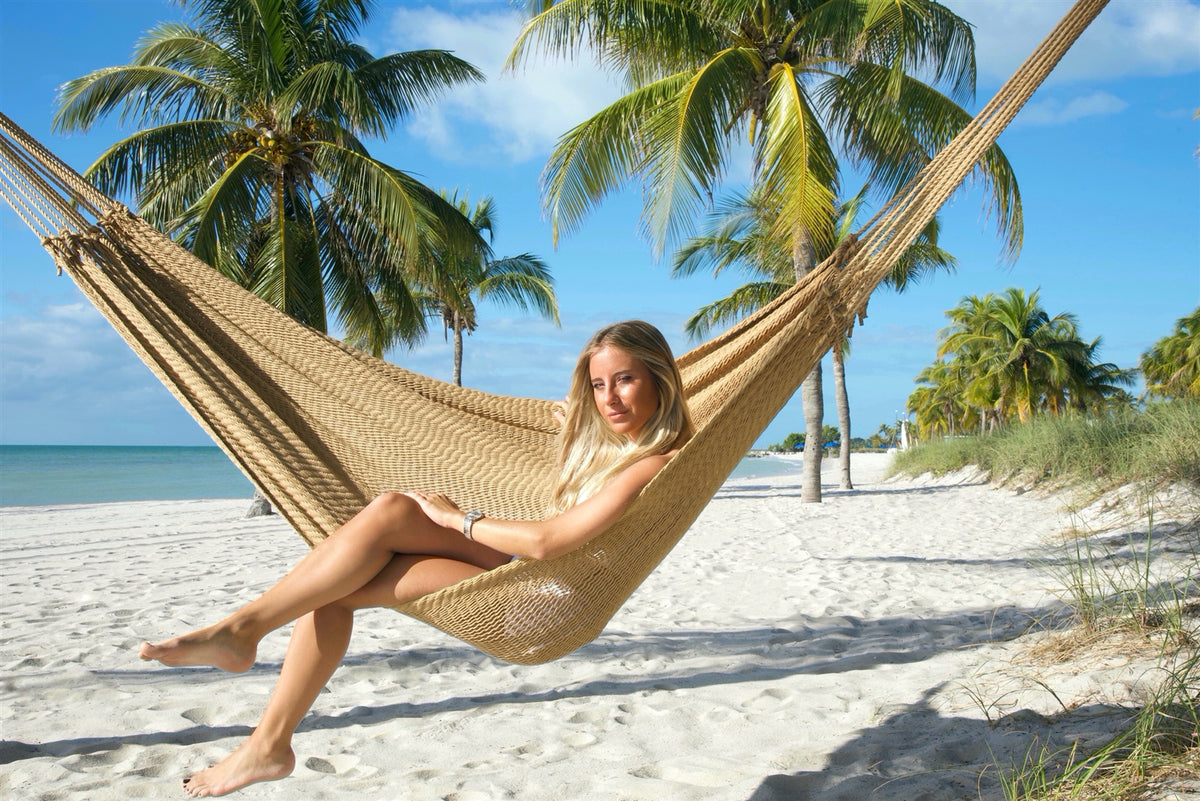 Woman sitting sideways in the Tan Jumbo Mayan Hammock with her legs crossed and feet reaching toward the sand
