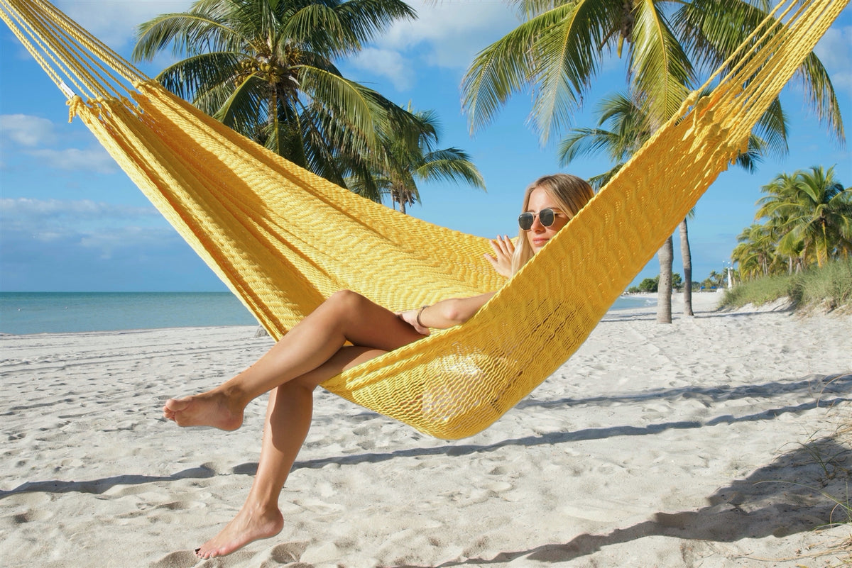 Woman sitting sideways in the Yellow Jumbo Mayan Hammock with her legs crossed, palm trees behind