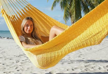 Woman lying back in the Yellow Jumbo Mayan Hammock, the deep bed cradling her on the beach