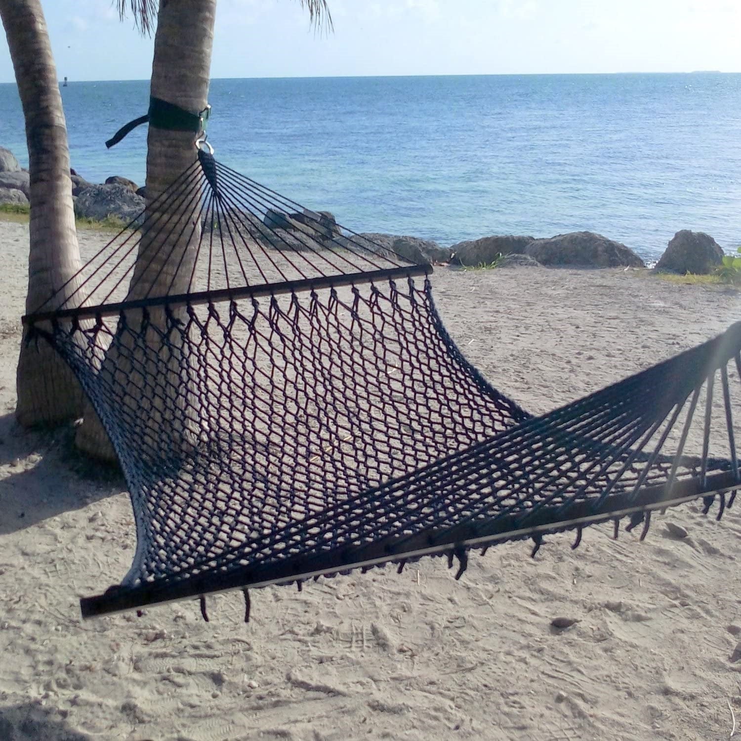 Black Jumbo Rope Hammock strung from a palm tree on a sandy Caribbean beach.
