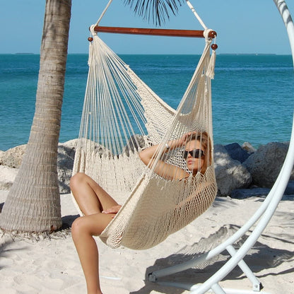 Woman seated in a cream Large Caribbean Hammock Chair on a white arc stand on a sandy beach
