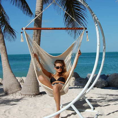 Woman relaxing in a cream Large Caribbean Hammock Chair on a white arc stand beneath palm trees by the ocean