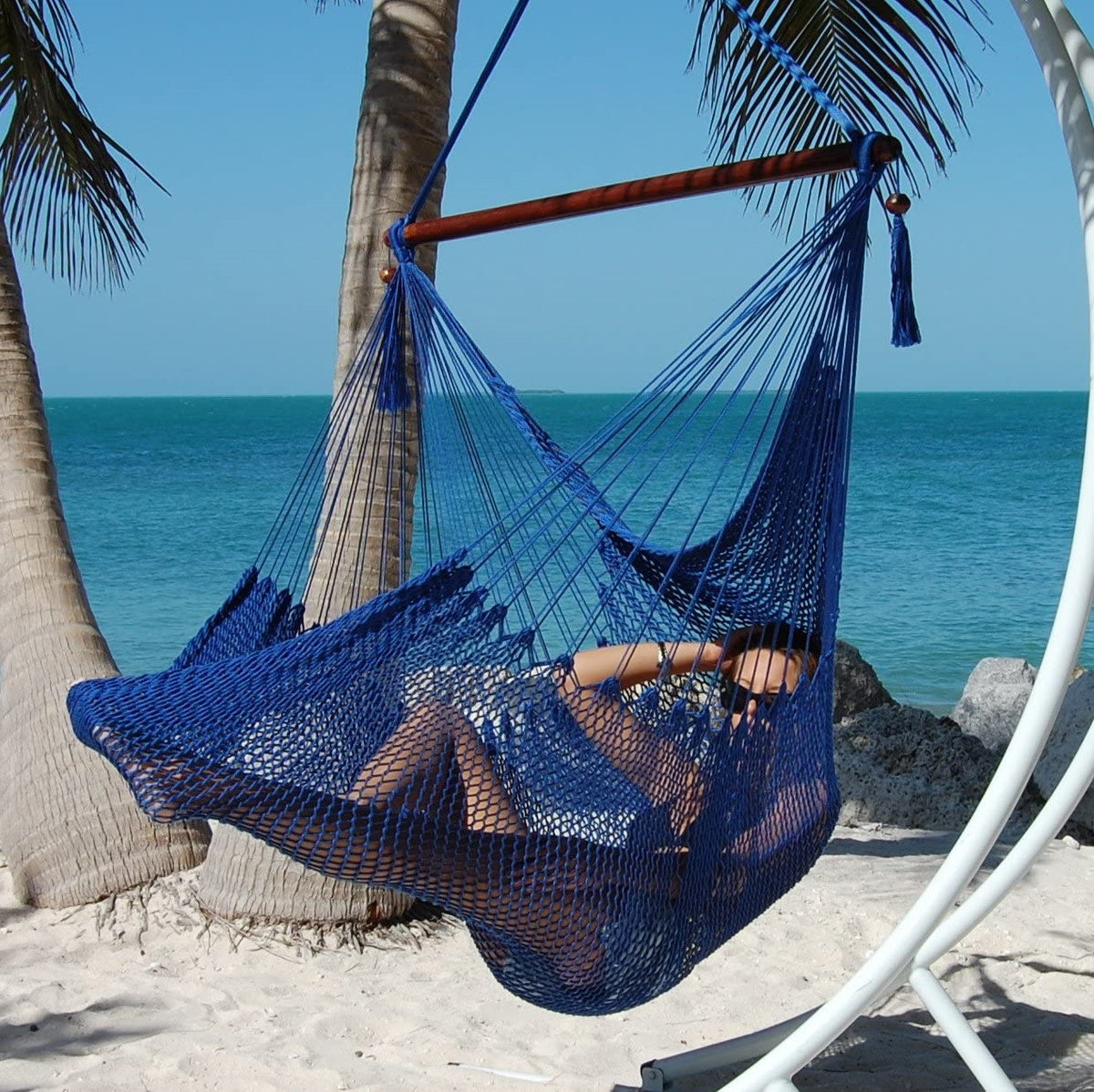 Woman reclining in a dark blue Large Caribbean Hammock Chair under palm trees on a white sand beach