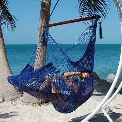 Woman reclining in a dark blue Large Caribbean Hammock Chair under palm trees on a white sand beach