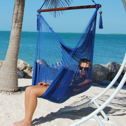 Woman relaxing in a dark blue Large Caribbean Hammock Chair on a white arc stand on a sandy beach