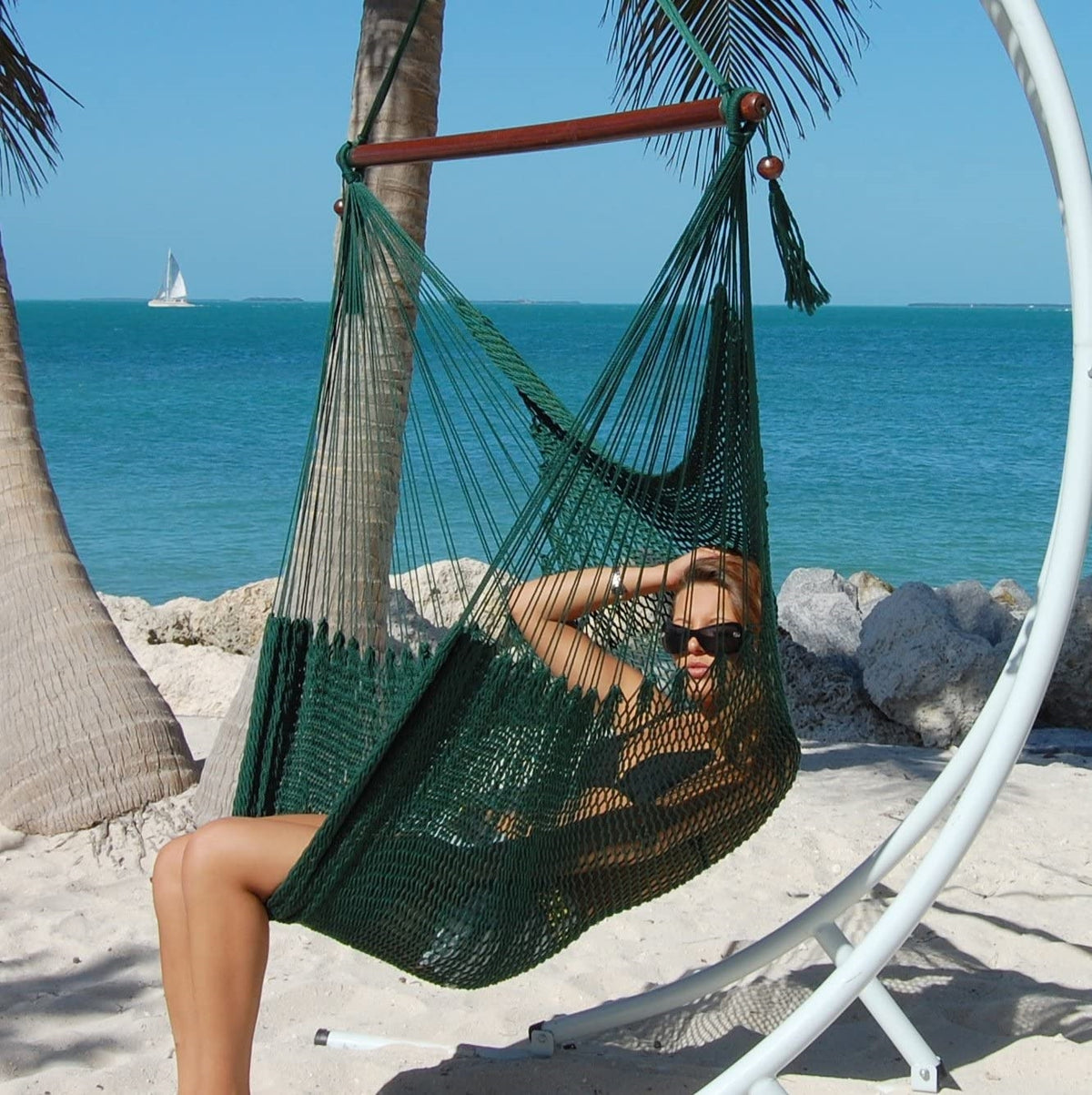 Woman reclining in a green Large Caribbean Hammock Chair on a white arc stand beside the ocean