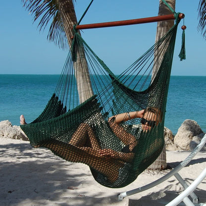 Woman relaxing in a green Large Caribbean Hammock Chair under palm trees on a white sand beach