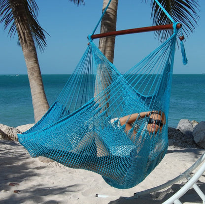Woman reclining in a light blue Large Caribbean Hammock Chair on a beach with palms and turquoise water behind