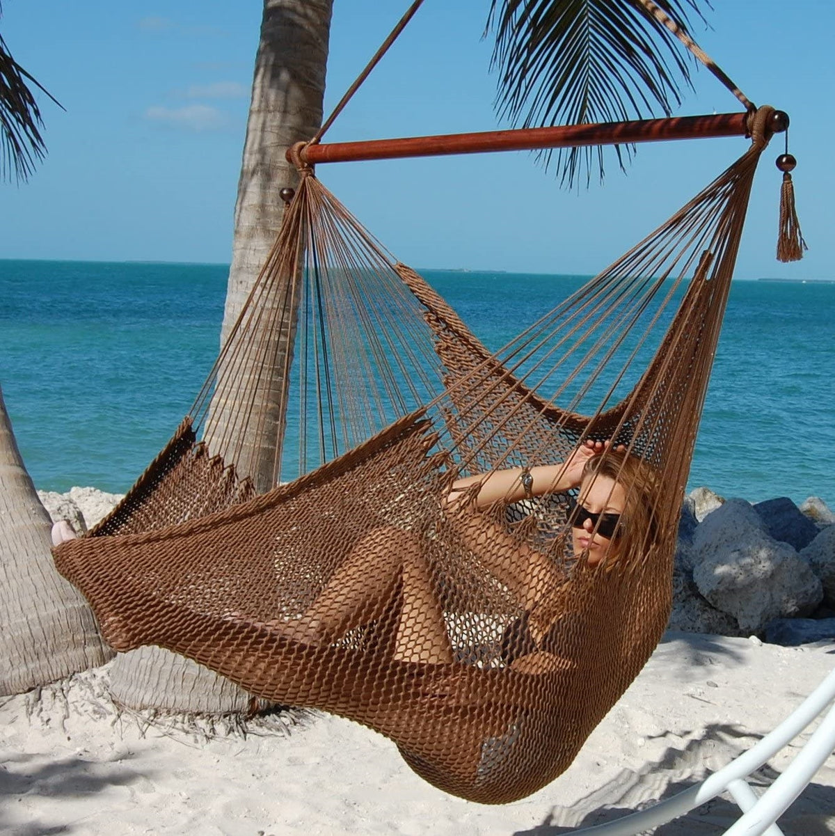 Woman reclining in a mocha Large Caribbean Hammock Chair under palm trees on a white sand beach