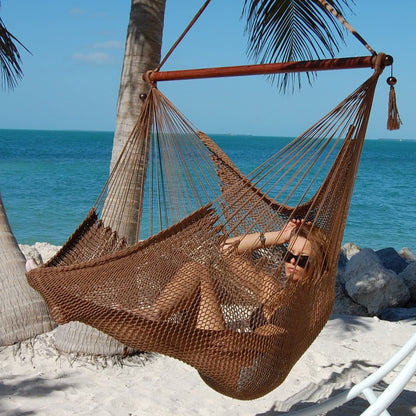 Woman reclining in a mocha Large Caribbean Hammock Chair under palm trees on a white sand beach