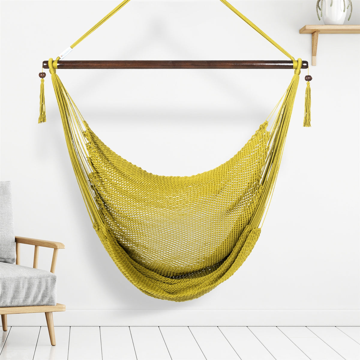 Olive Large Caribbean Hammock Chair hanging indoors beside a pale wood armchair against a white wall