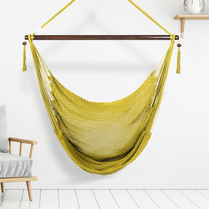 Olive Large Caribbean Hammock Chair hanging indoors beside a pale wood armchair against a white wall