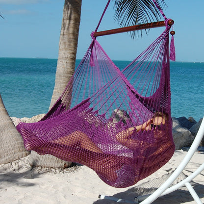 Woman reclining in a purple Large Caribbean Hammock Chair on a white arc stand beside palm trees and the ocean