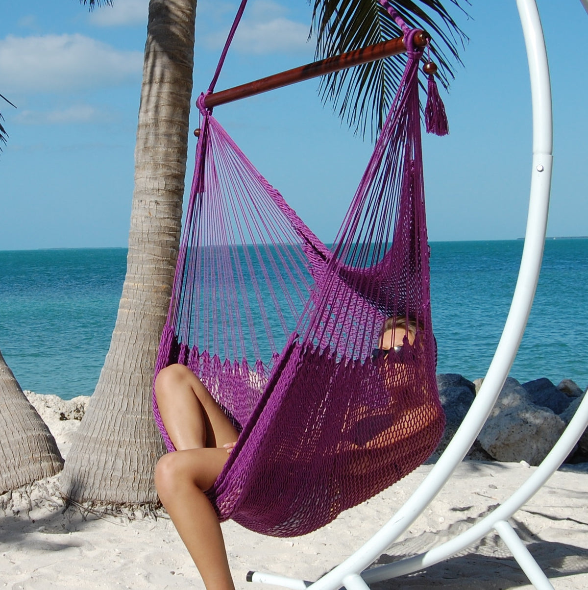 Woman relaxing in a purple Large Caribbean Hammock Chair on a white arc stand beneath palm trees by the ocean