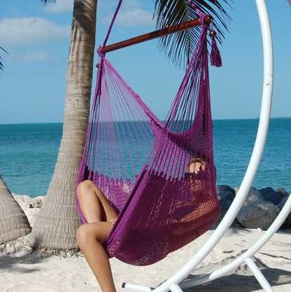 Woman relaxing in a purple Large Caribbean Hammock Chair on a white arc stand beneath palm trees by the ocean
