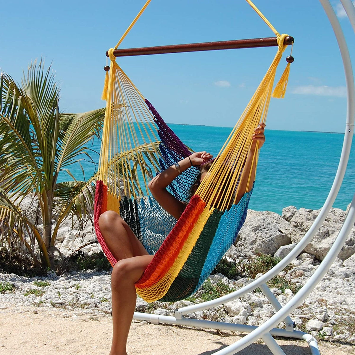 Woman relaxing with her legs up in a rainbow Large Caribbean Hammock Chair with yellow end cords beside the ocean