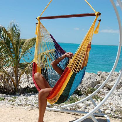 Woman relaxing with her legs up in a rainbow Large Caribbean Hammock Chair with yellow end cords beside the ocean
