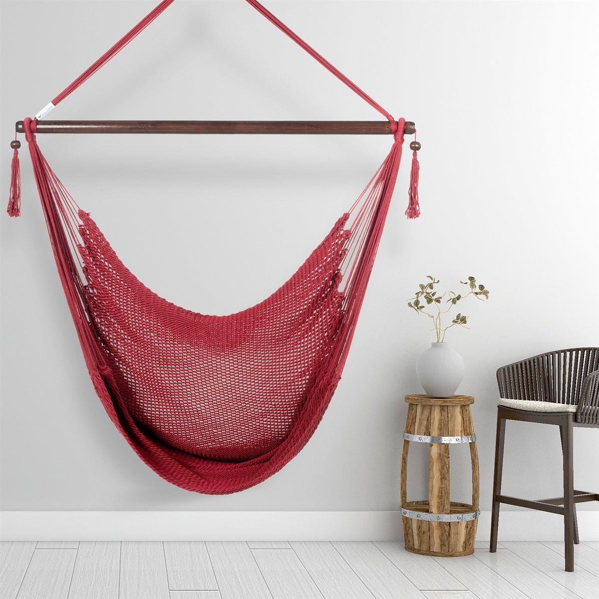 Red Large Caribbean Hammock Chair hanging beside a barrel side table and rattan stool against a pale grey wall
