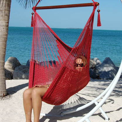 Woman seated in a red Large Caribbean Hammock Chair on a white arc stand on a sandy beach