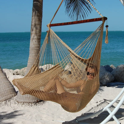 Woman reclining in a tan Large Caribbean Hammock Chair on a white arc stand beside palm trees and the ocean