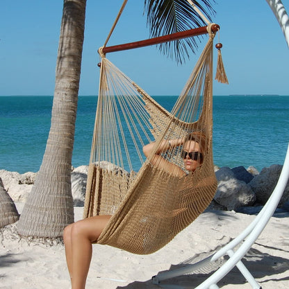 Woman relaxing in a tan Large Caribbean Hammock Chair on a white arc stand beneath palm trees by the ocean