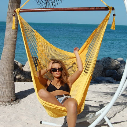 Woman seated in a yellow Large Caribbean Hammock Chair on a white arc stand beside palm trees and the ocean
