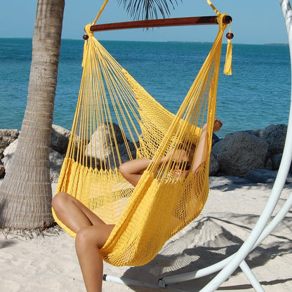 Woman relaxing in a yellow Large Caribbean Hammock Chair on a white arc stand overlooking the ocean